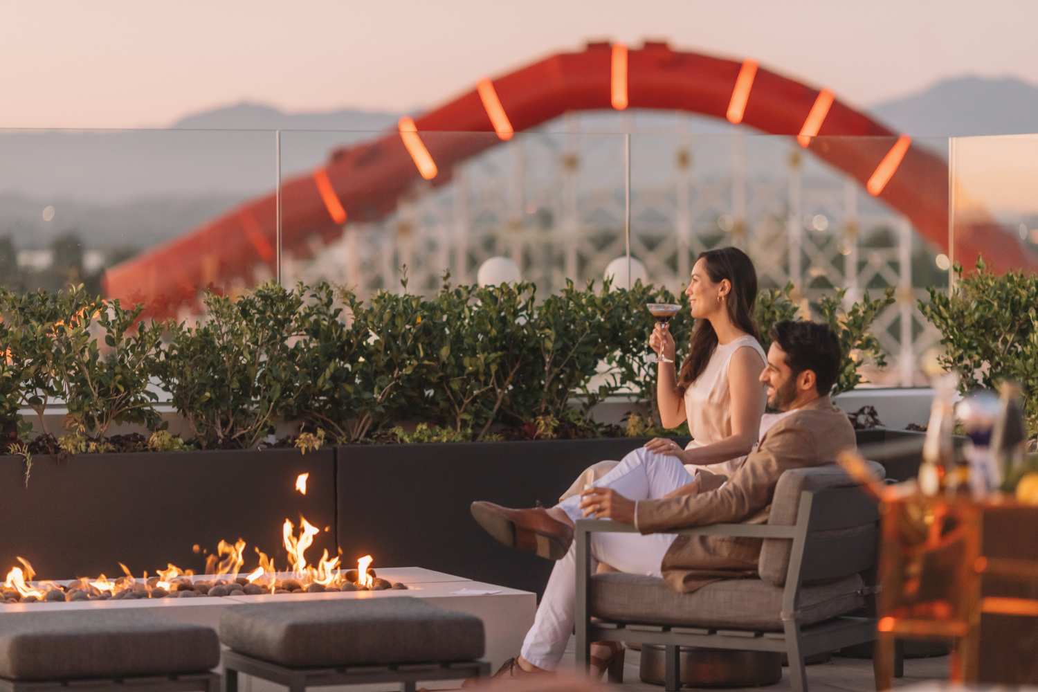 man and woman sitting on a rooftop in front of a lit fire pit