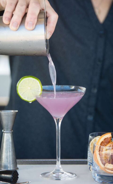bartender pouring a cocktail into a martini glass