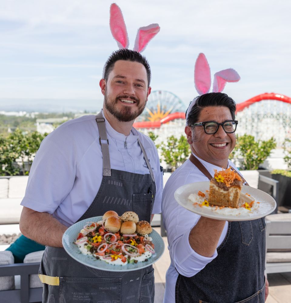 Two chefs wearing bunny ears, holding plated dishes outdoors.
